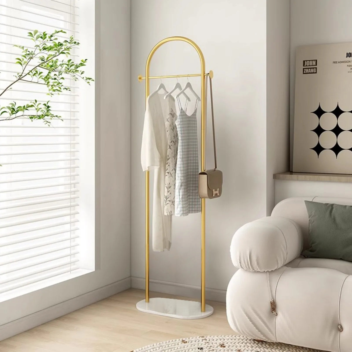 Porte-vêtements en arche doré avec socle ovale blanc, robes sur cintres et sac suspendu