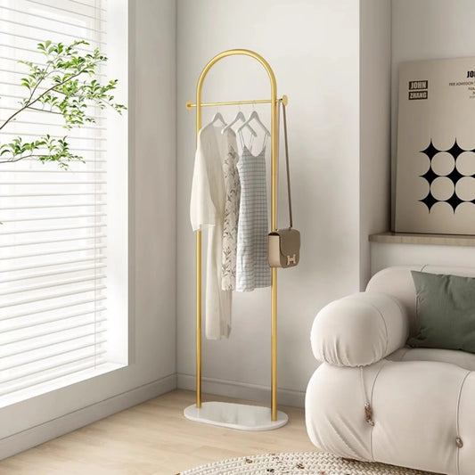 Porte-vêtements en arche doré avec socle ovale blanc, robes sur cintres et sac suspendu