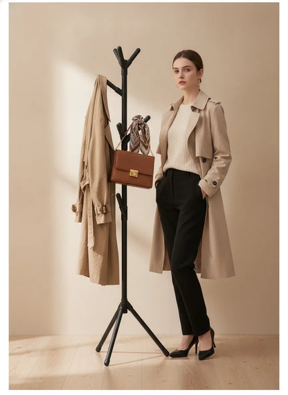 Femme en trench à côté d'un porte-vêtements noir sur trépied avec manteau et sac